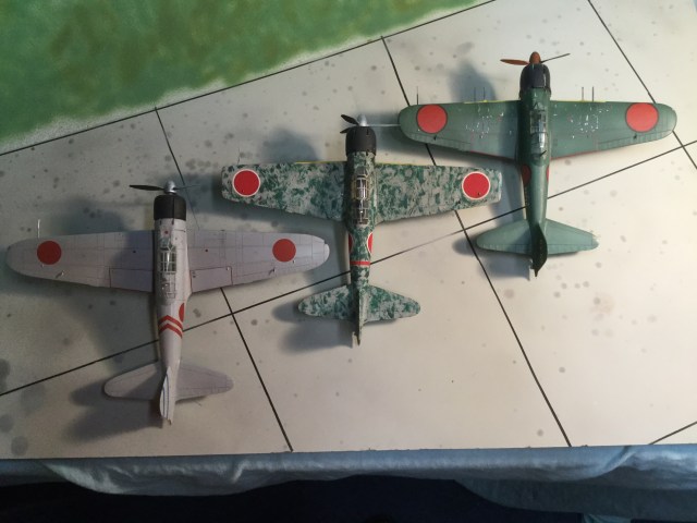 This overhead shows three major types of Zero. The A6M2 Model 21 is on the left (a model 11 was built in small numbers with the same wing shape, but no folding tips). The A6M3 Model 32 shows the new squared tips, and the enlarged engine. Also, the 20 mm cannon in the wings were an improved type with a better rate of fire. The A6M5 Model 52c right is the final major version. The wing has the same span as the Model 32 but the tips have been rounded. It also has an even more improved 20 mm cannon and a heavy machine gun in each wing. But it still uses the same engine.